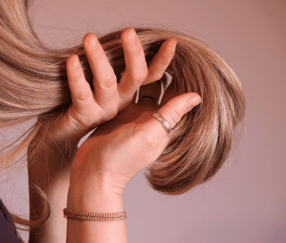 A woman's hand touching her blond hair against a pink background.