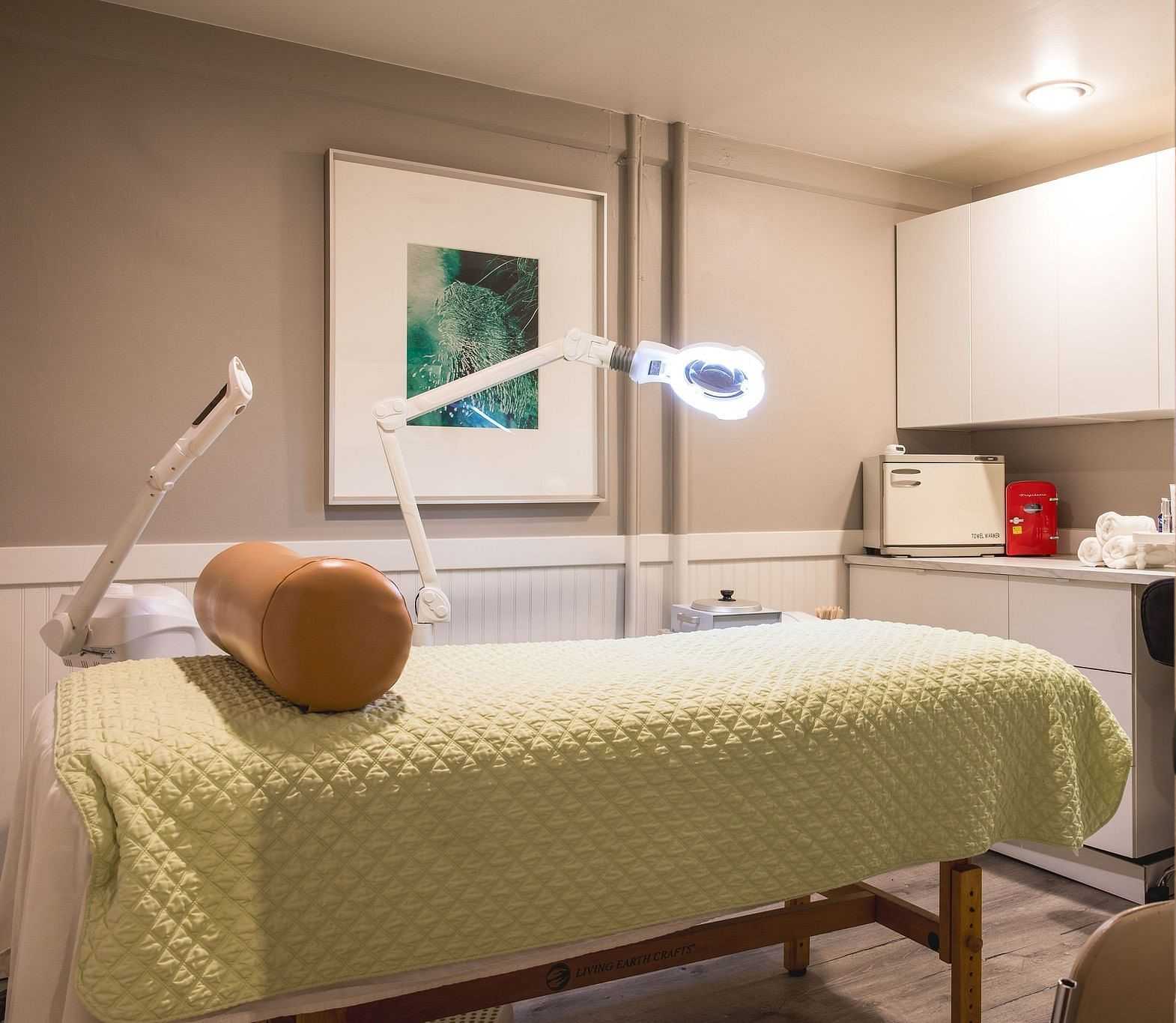 Treatment room with a massage table, lamp, and medical equipment on a counter.