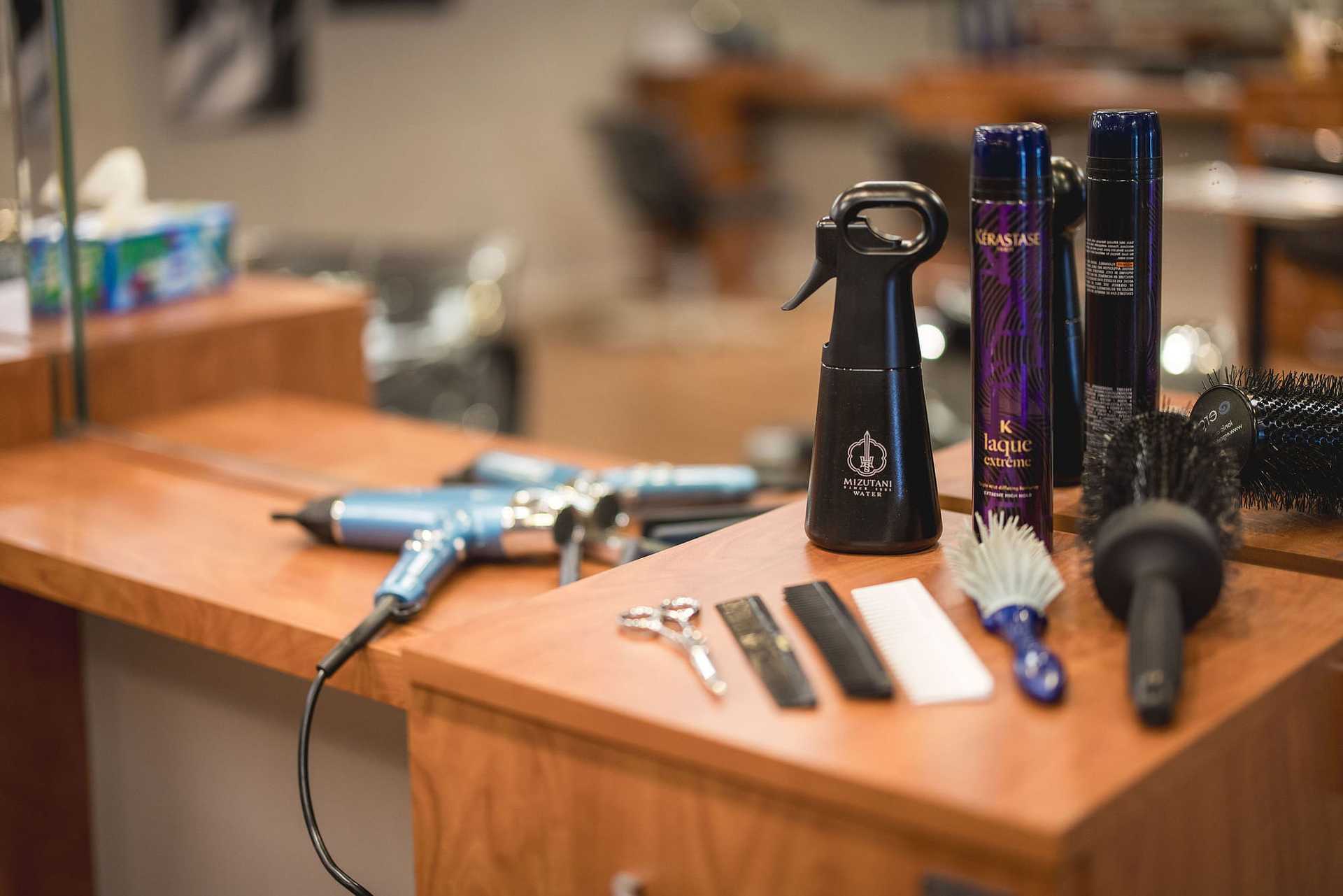 Hair styling tools on a salon counter: sprays, combs, brushes, scissors, and curling irons.